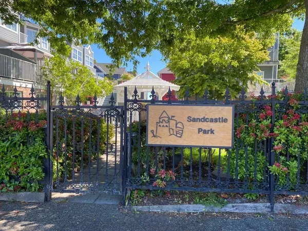The wooden Sandcastle Park sign on a black iron fence, with trees and a white gazebo behind it