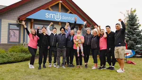 The Smili Dental team cheering with raised fists outside a clinic under its blue sign
