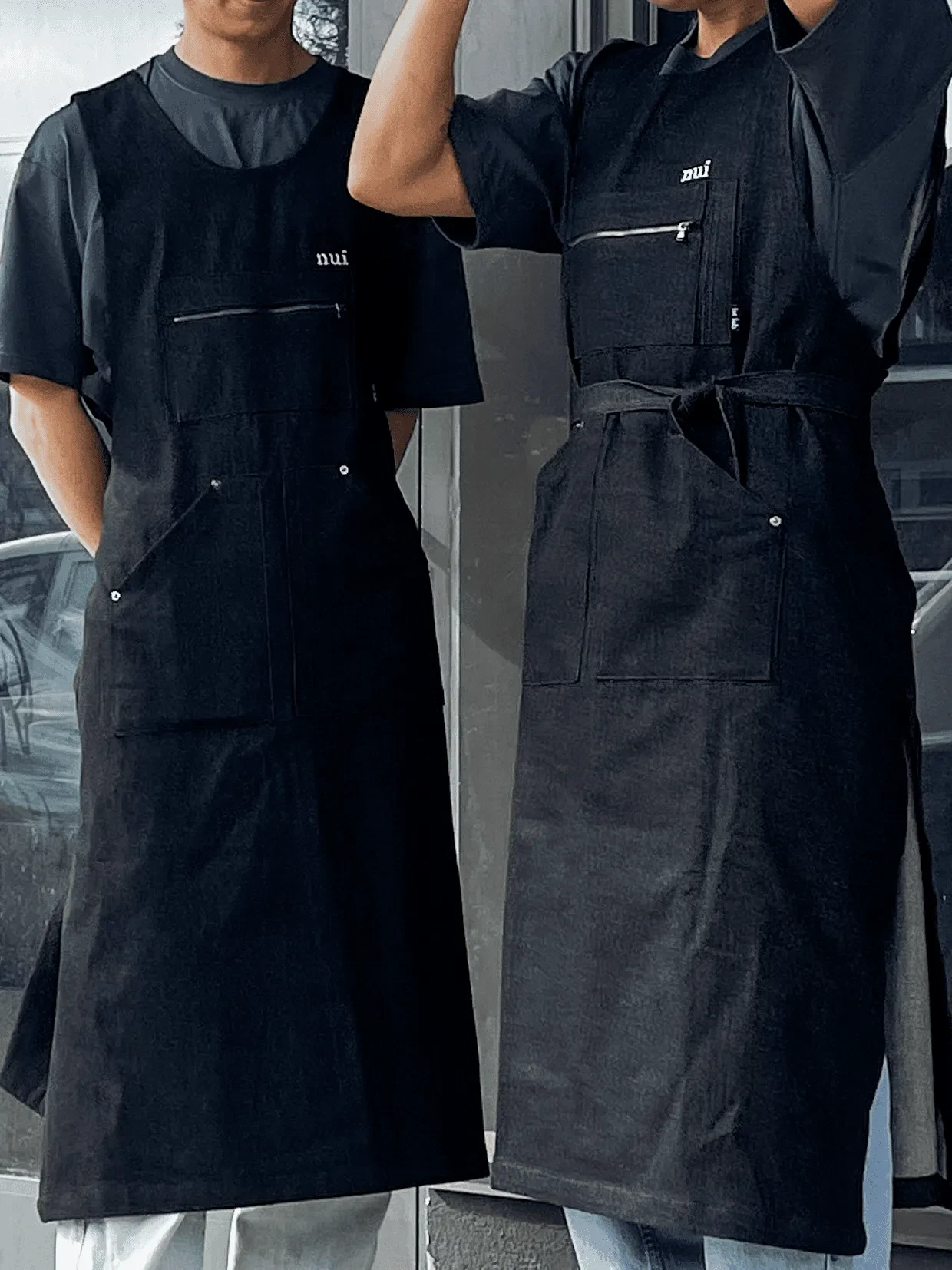 Two staff in black aprons embroidered with the Nui logo, standing in front of a window