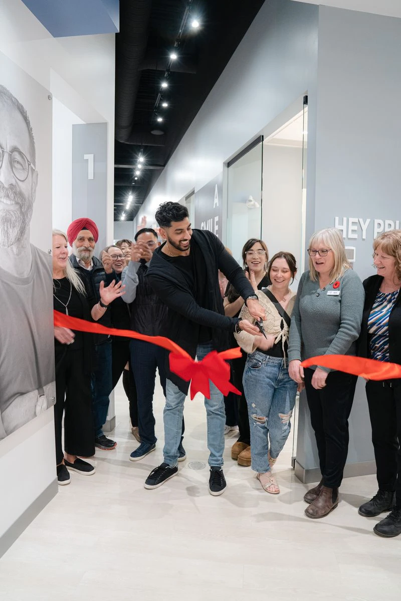 A smiling man cutting a red ribbon with scissors as staff and guests cheer in a dental clinic hallway