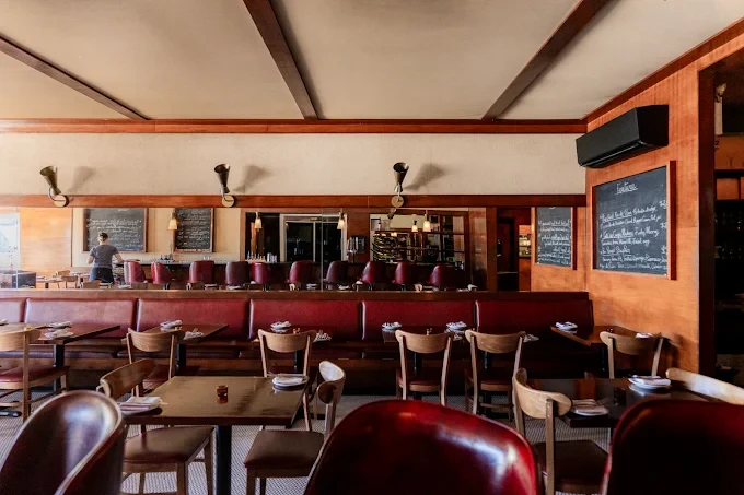 The Les Faux Bourgeois dining room: wooden tables and chairs in front of a long red leather banquette, with chalkboard menus on the walls